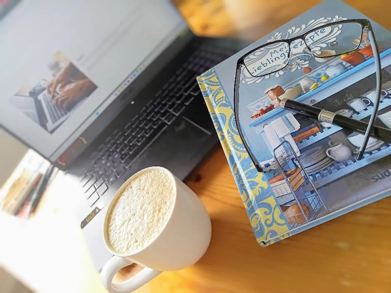 HEYNER- Buch, Stift und Brille vor Laptop mit Kaffee platziert